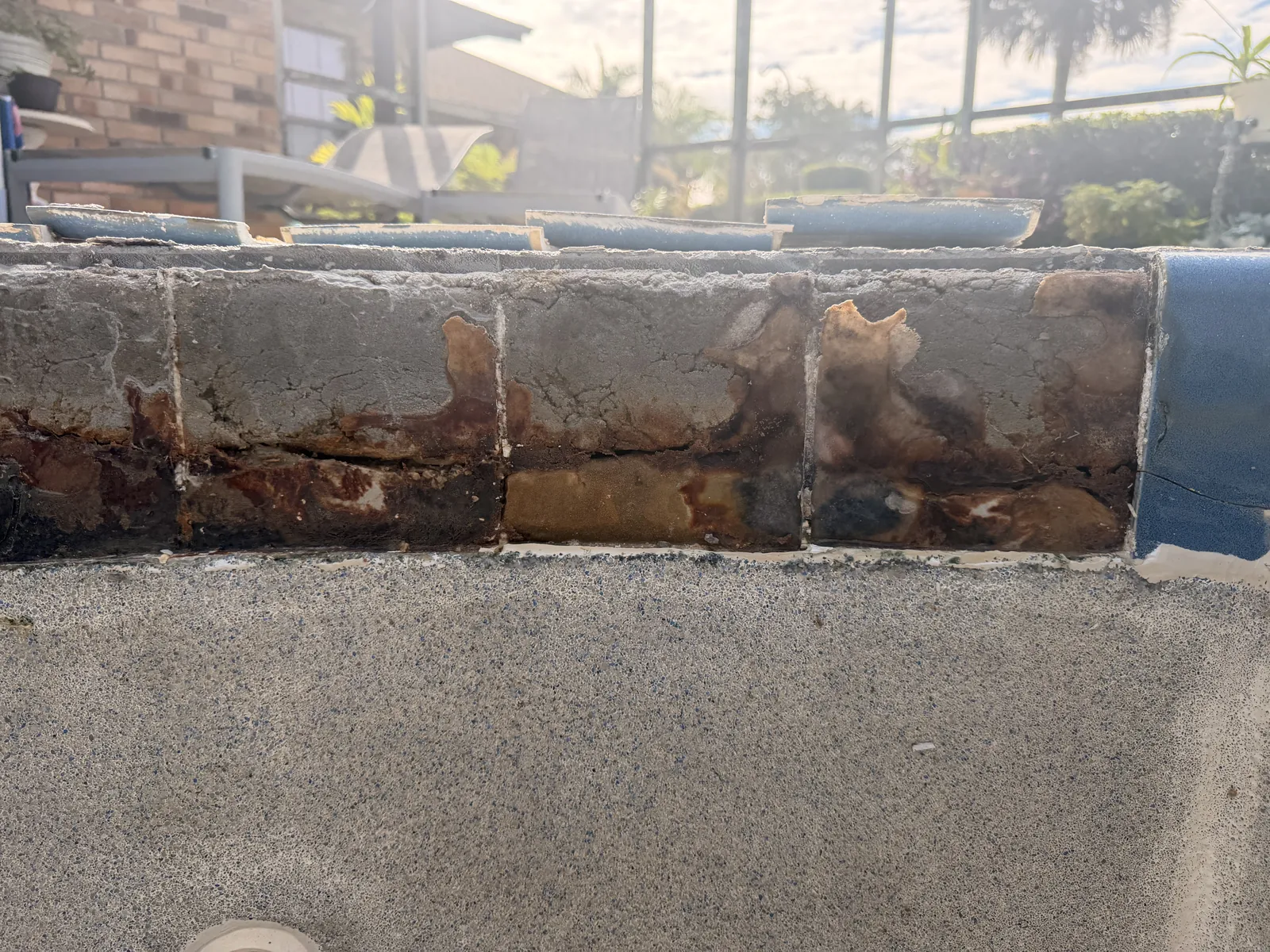 Close-up of cracked, separated and rust-stained spa tile along the bond beam — Deltona, FL