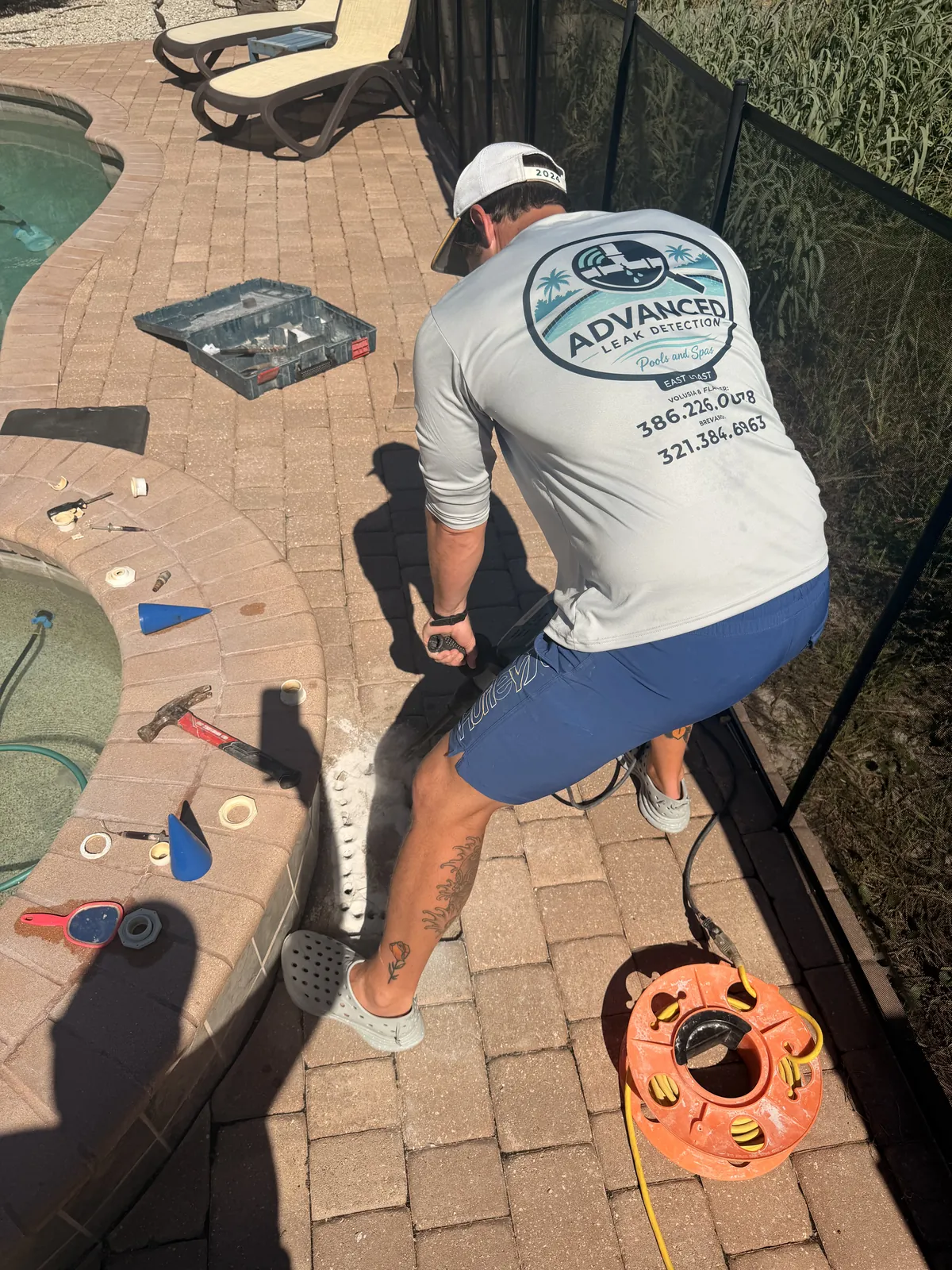Technician chipping through the concrete slab under the pavers beside a spa to reach a therapy jet leak — Palm Coast, FL